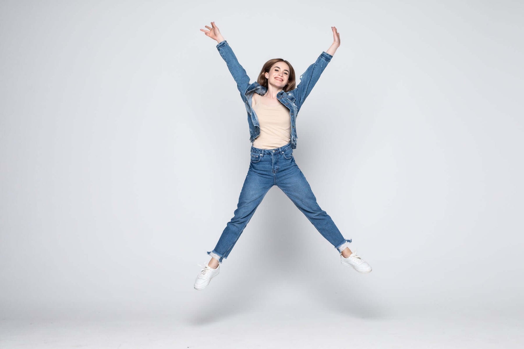 Woman jumping in denim jacket and jeans against grey background
