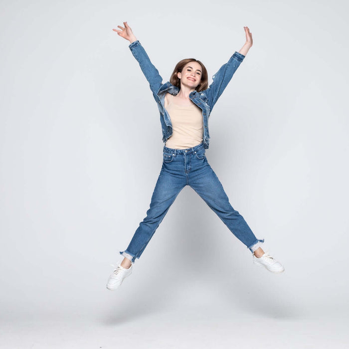 Woman jumping in denim jacket and jeans against grey background